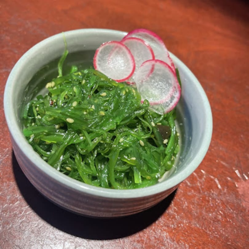 Mikado Ryotei's vibrant green seaweed salad with sesame seeds and thinly sliced radishes in a bowl.
