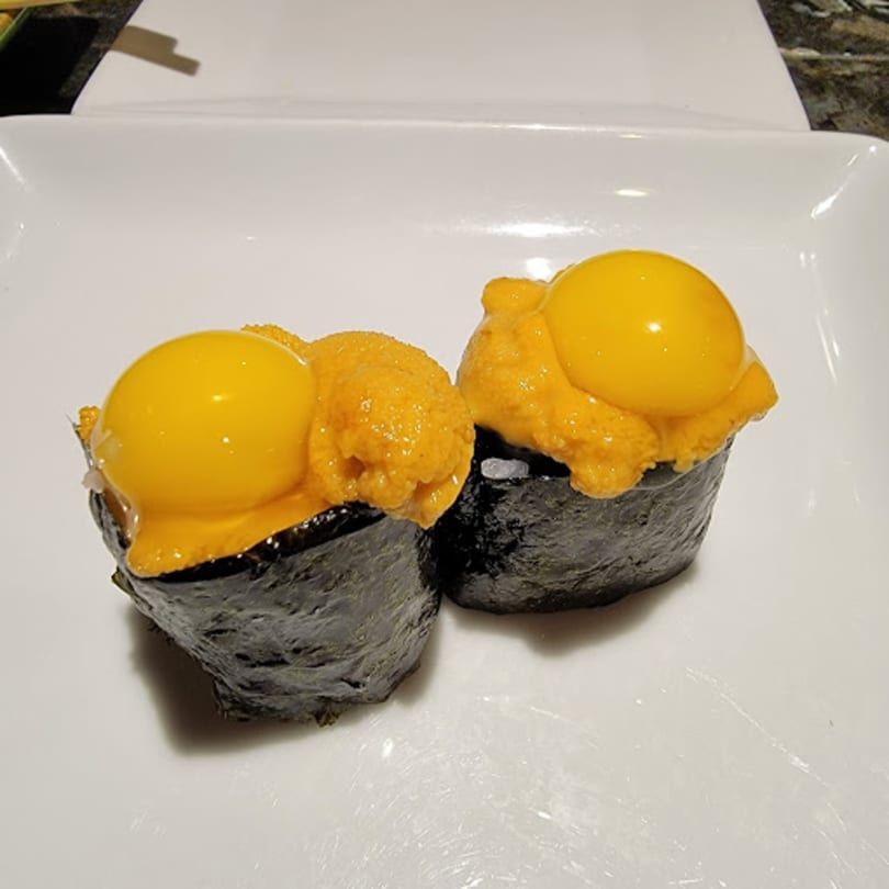 Two Mikado Ryotei uni sushi pieces, each topped with a bright yellow quail egg yolk.